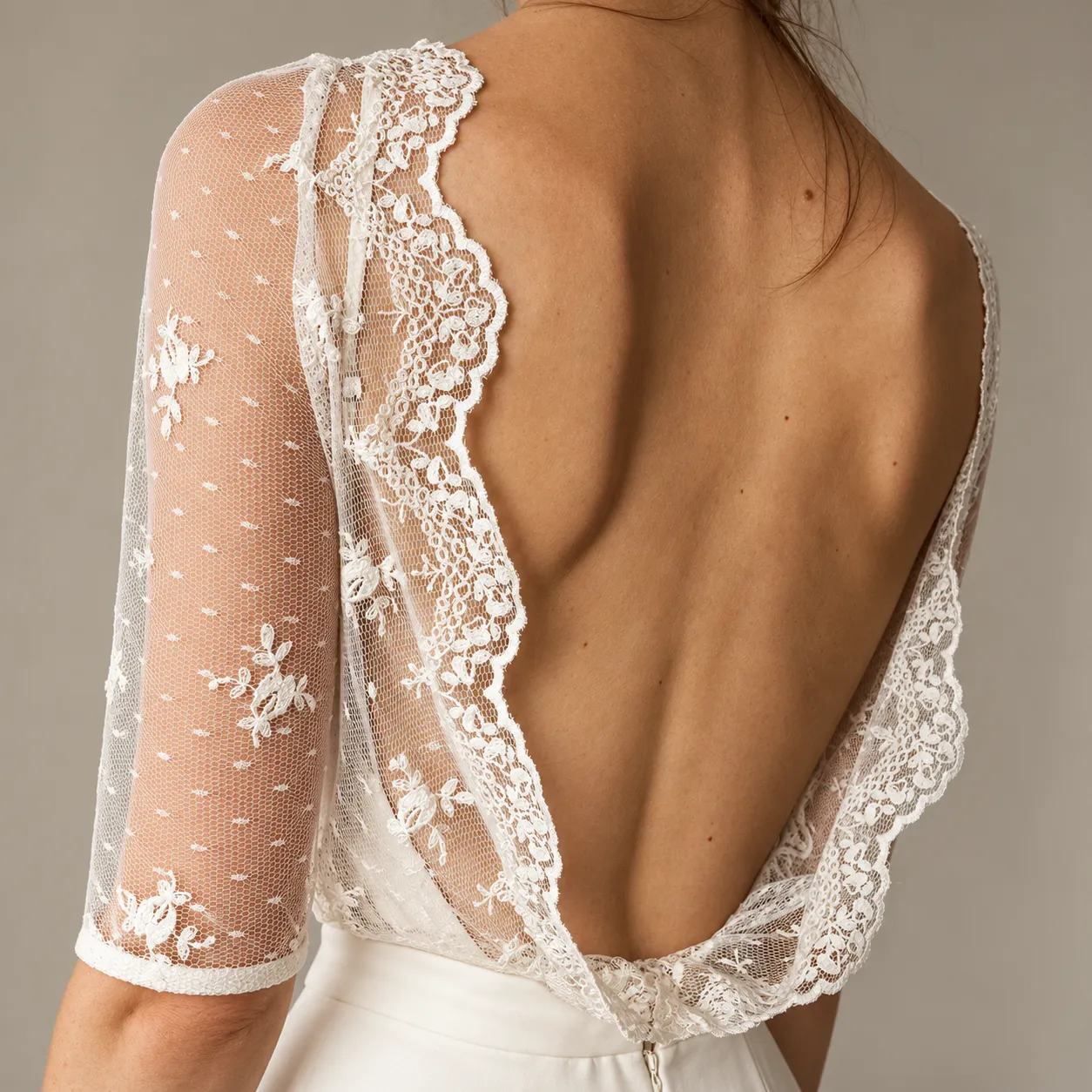 The open back of a custom gown up close — scalloped ivory lace edging a deep V, sheer embroidered sleeves