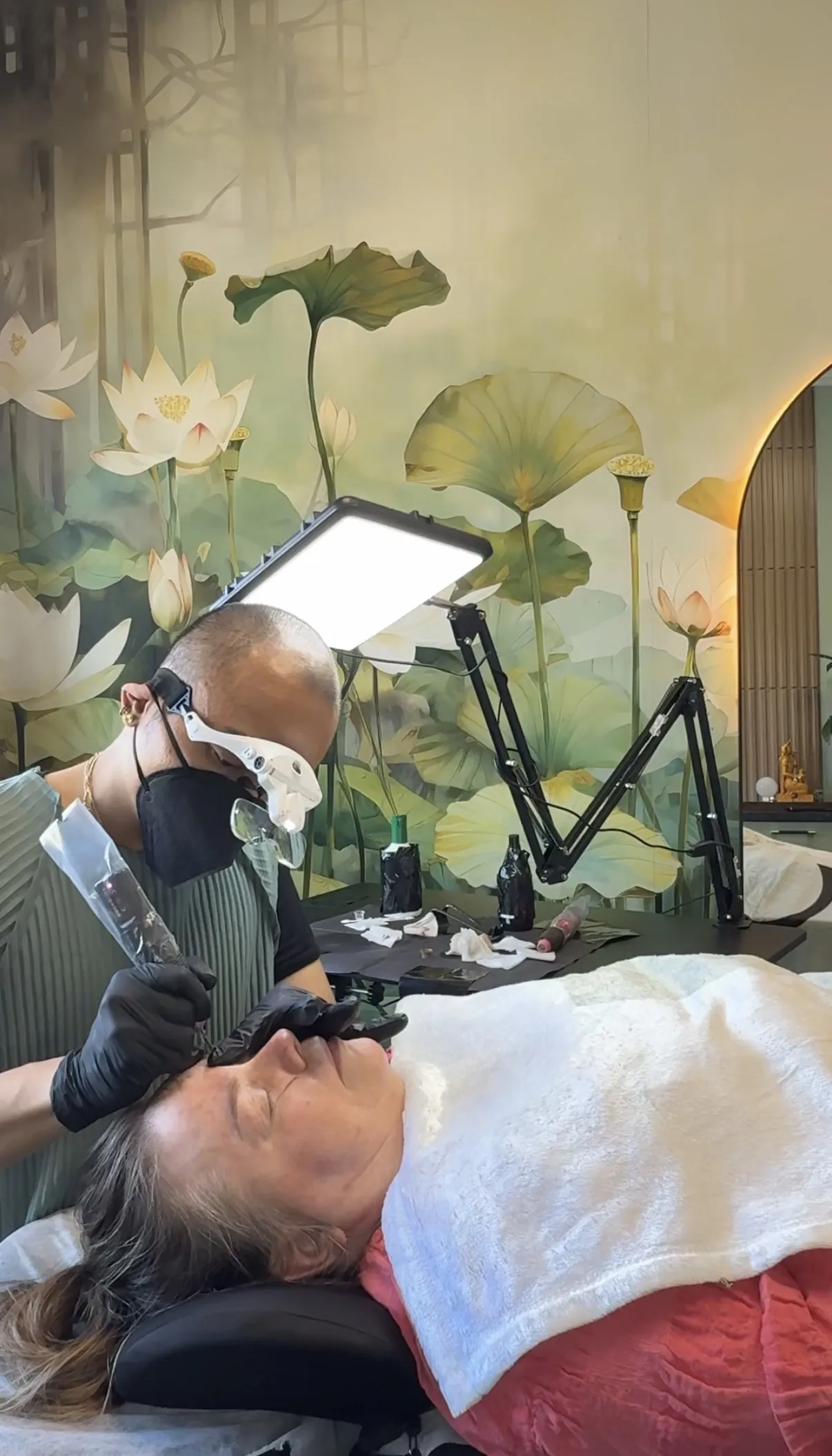 David at work on a client's brows in the DCPC studio, under a lotus mural