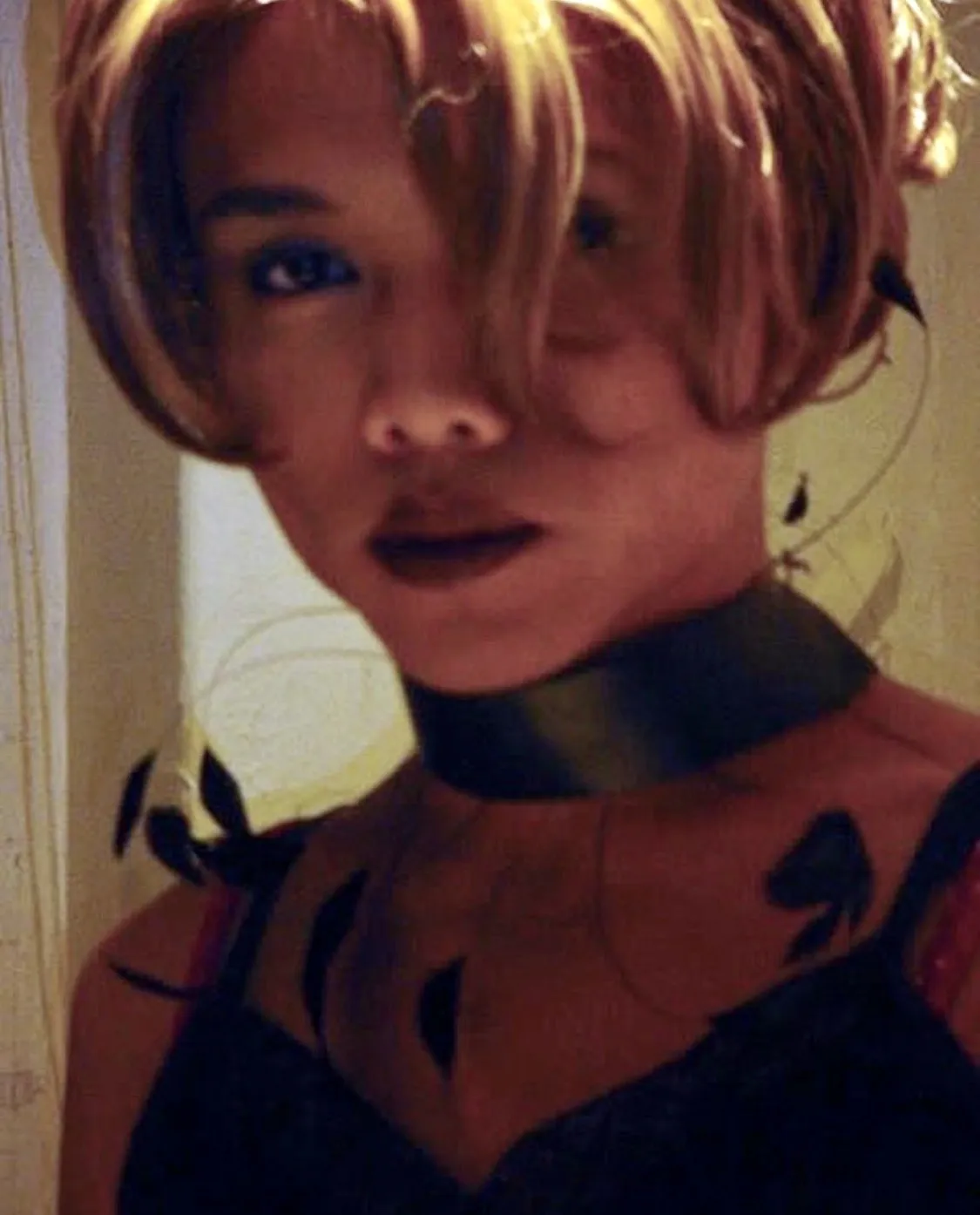 An early drag photograph of David — a short blonde wig, dark lips, a black choker and black feathered dress