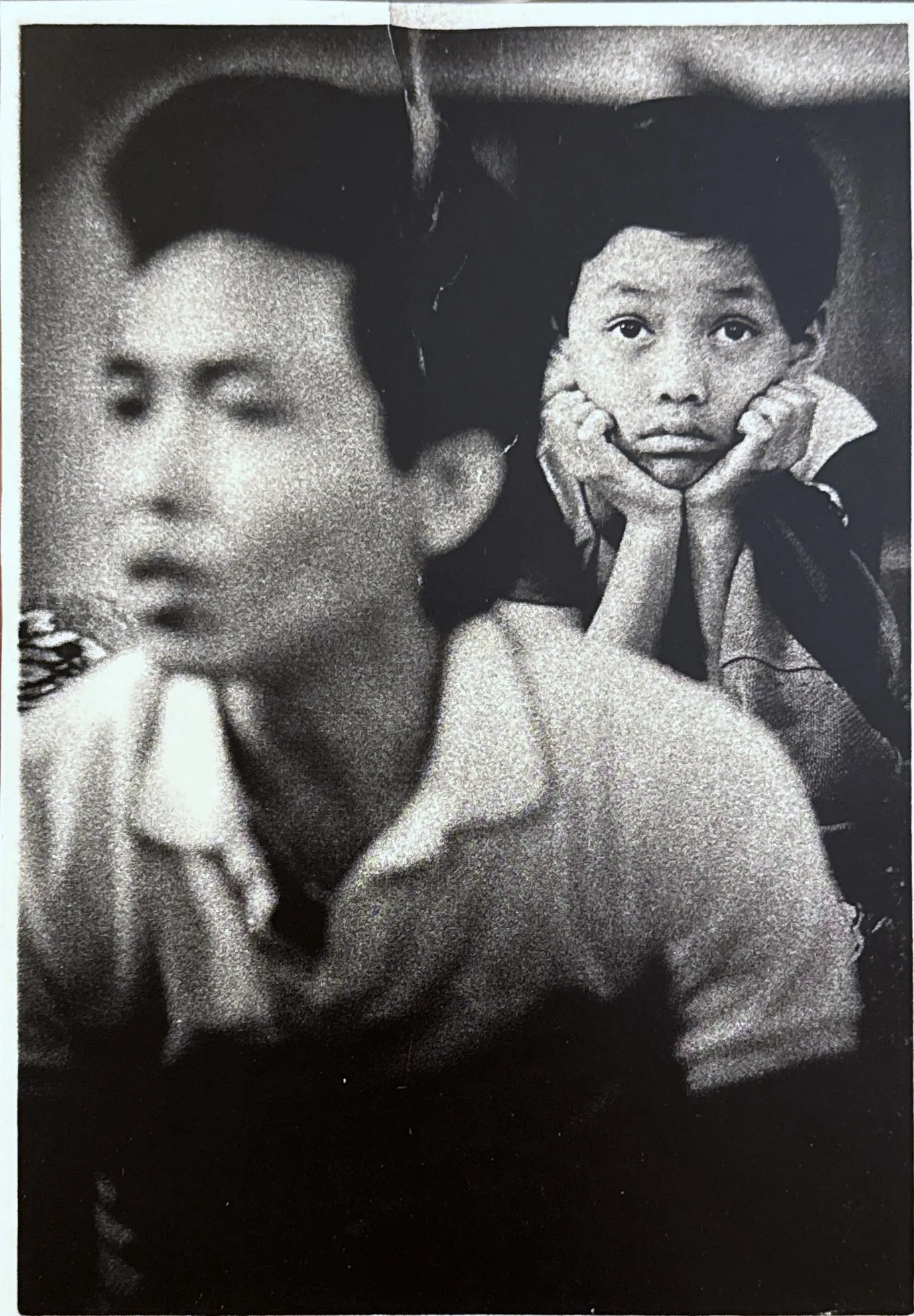 A grainy black-and-white family photograph — a man in a light shirt in the foreground, a boy behind him resting his chin in both hands