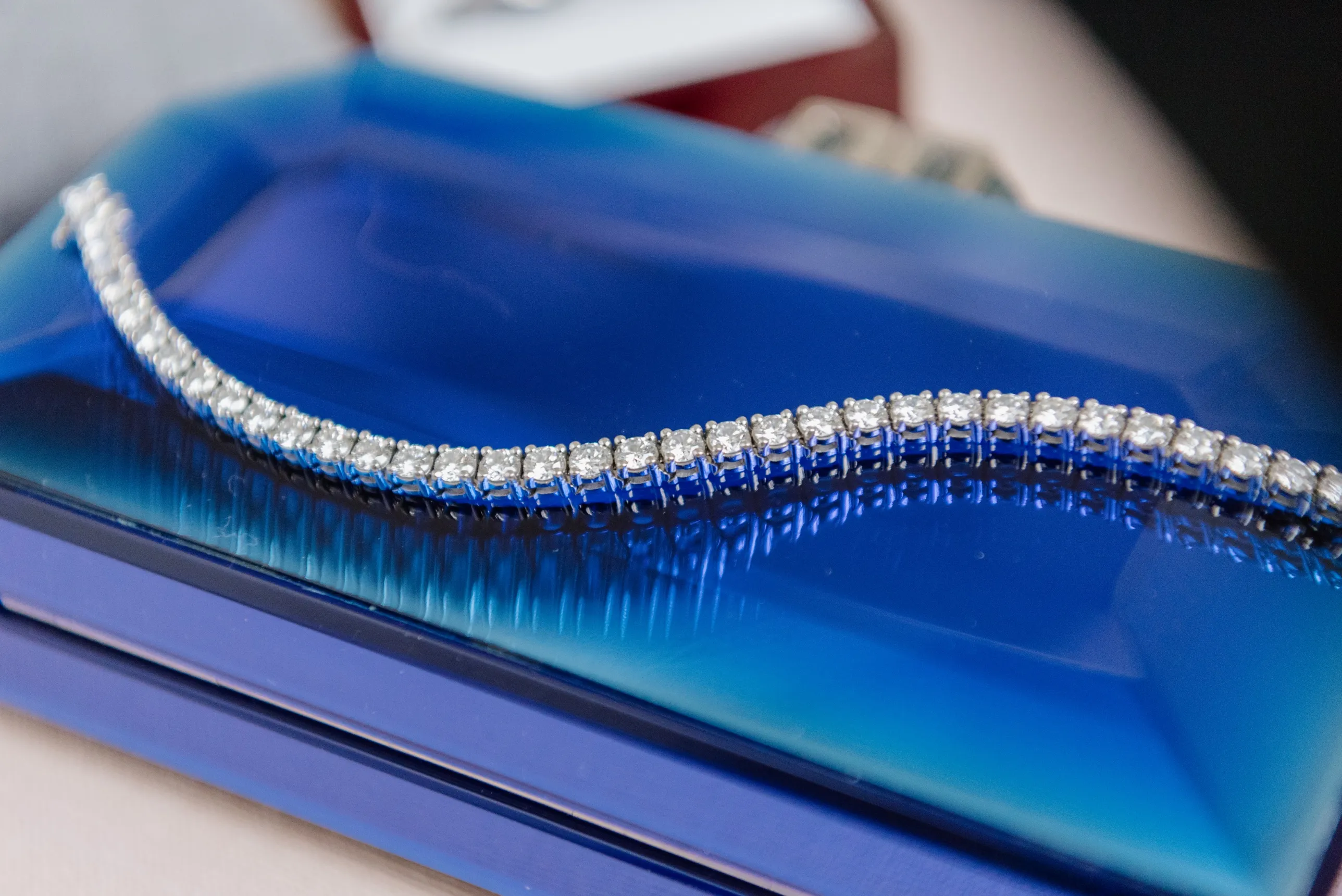A diamond tennis bracelet curving across a lacquered cobalt-blue jewellery box